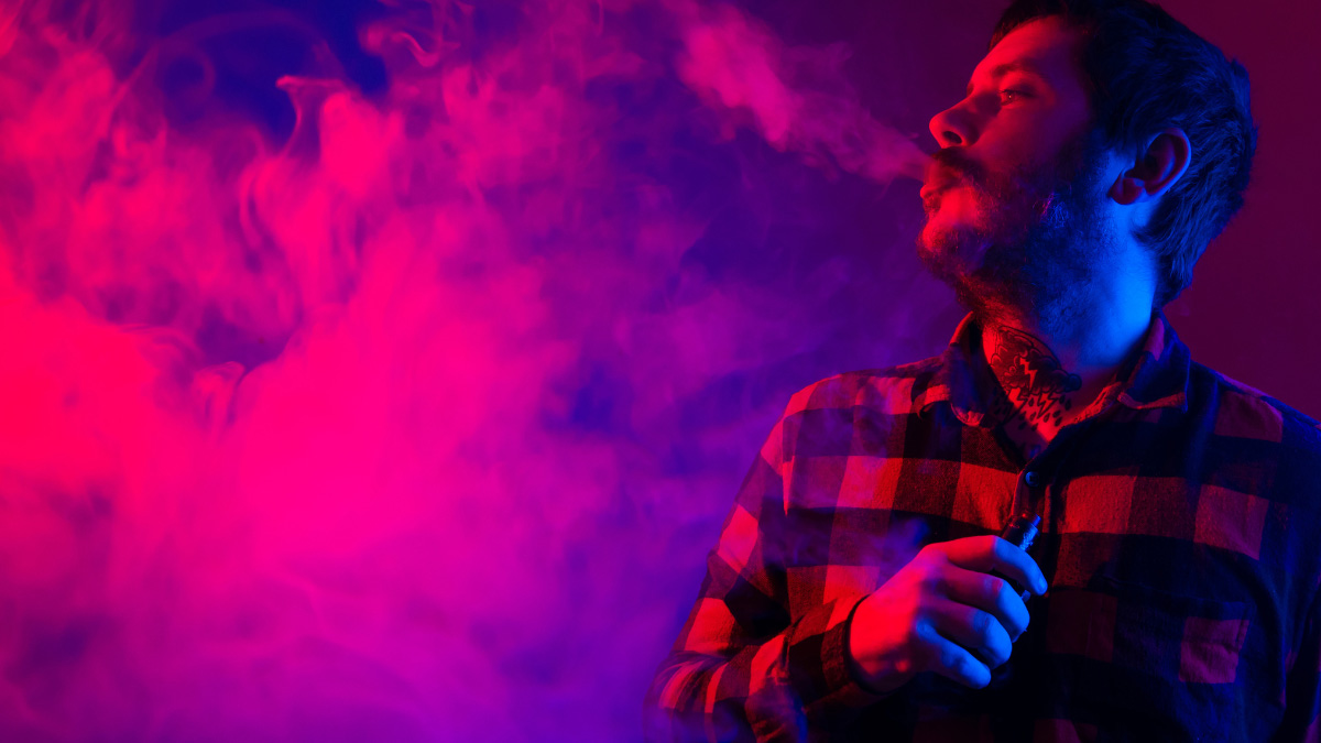 A man wearing a checkered shirt turning his head to the side and blowing out vapor from a THCa Vape near Garland, Texas.